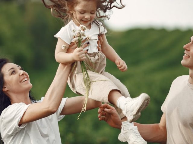 Happy family enjoying playful outdoor moment, lifting child in summer day.
